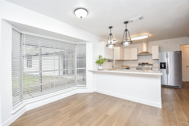 kitchen with white cabinetry, sink, stainless steel appliances, wall chimney range hood, and decorative light fixtures