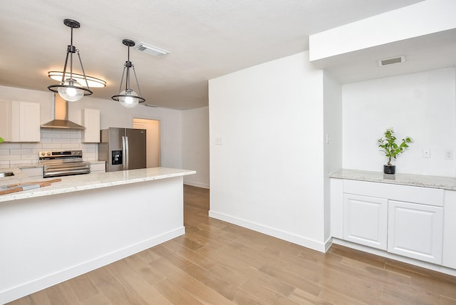 kitchen featuring light stone countertops, appliances with stainless steel finishes, tasteful backsplash, wall chimney range hood, and white cabinets