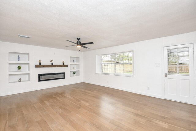 unfurnished living room featuring a textured ceiling, built in features, ceiling fan, and a healthy amount of sunlight