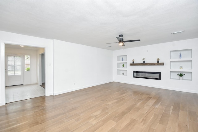 unfurnished living room featuring built in shelves, a textured ceiling, hardwood / wood-style flooring, and ceiling fan