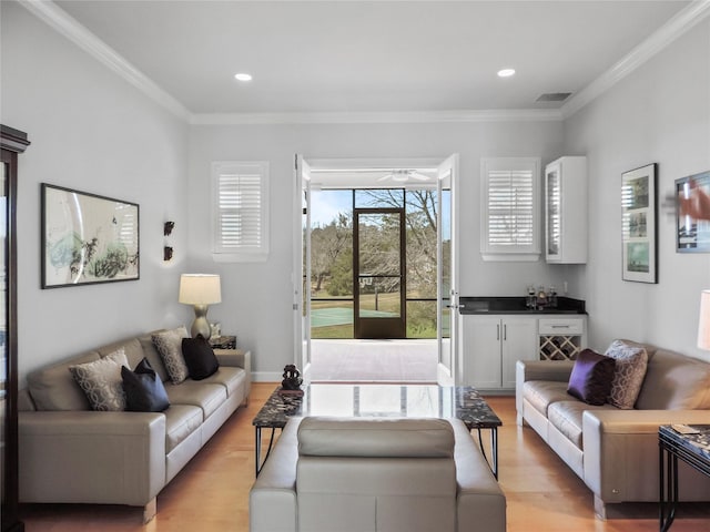 living room with ceiling fan, light wood-type flooring, ornamental molding, and bar