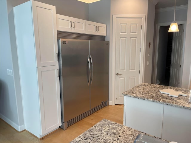 kitchen with light stone countertops, pendant lighting, light hardwood / wood-style flooring, white cabinetry, and stainless steel refrigerator