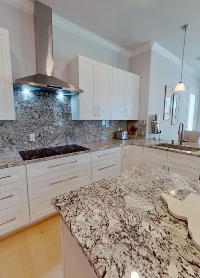 kitchen with white cabinetry, sink, hanging light fixtures, wall chimney range hood, and backsplash