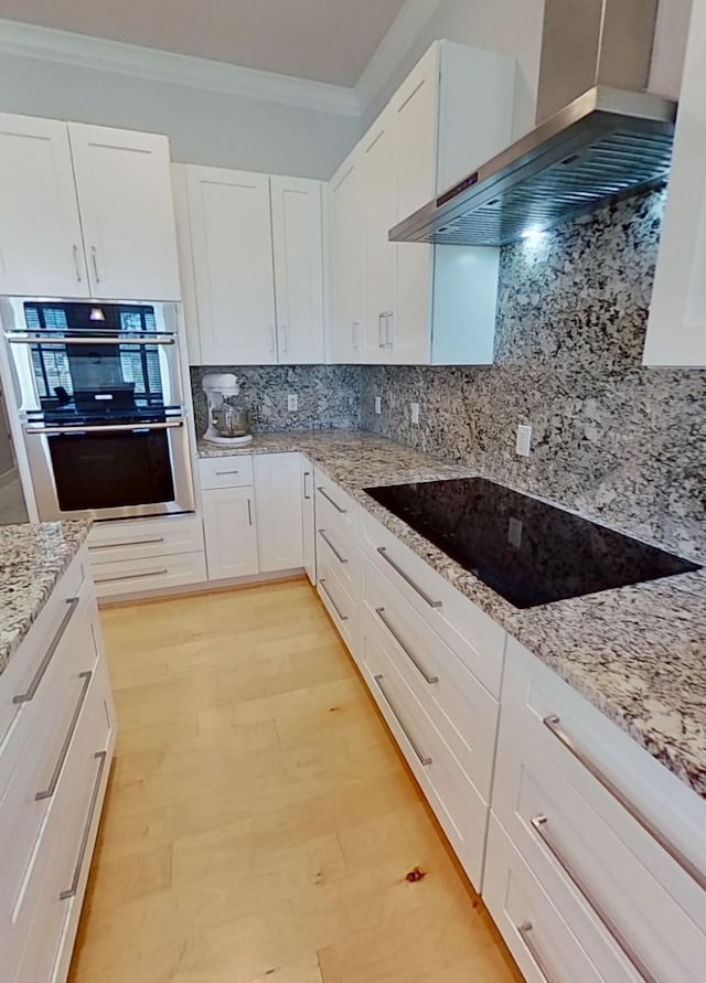 kitchen with backsplash, white cabinets, black electric stovetop, wall chimney exhaust hood, and double oven