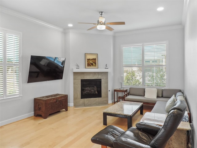 living room featuring hardwood / wood-style floors, ceiling fan, ornamental molding, and a tile fireplace