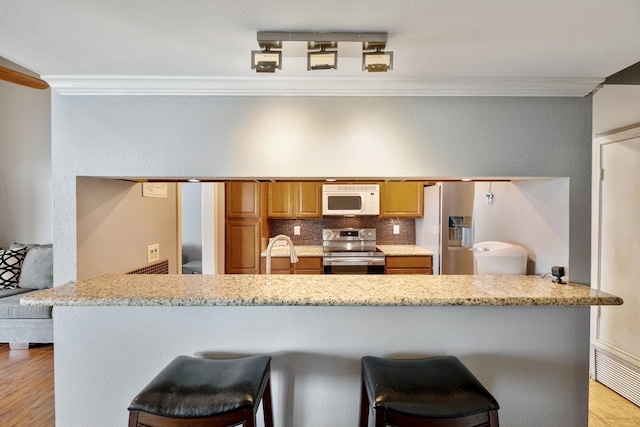 kitchen featuring decorative backsplash, kitchen peninsula, stainless steel appliances, crown molding, and a breakfast bar area