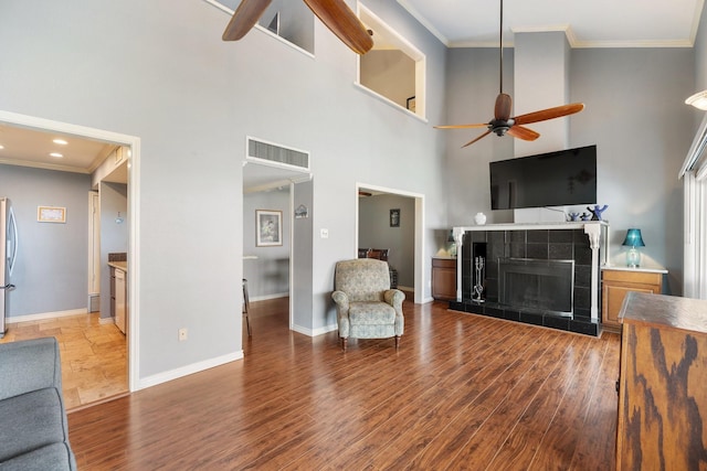 living room with a tile fireplace, hardwood / wood-style floors, a towering ceiling, and ornamental molding