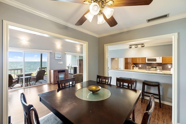 dining space featuring hardwood / wood-style floors, ceiling fan, a water view, and crown molding