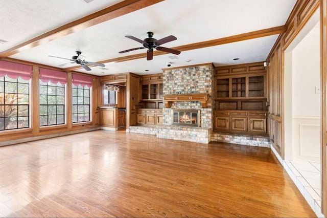 unfurnished living room with beam ceiling, ceiling fan, built in features, light hardwood / wood-style floors, and a fireplace