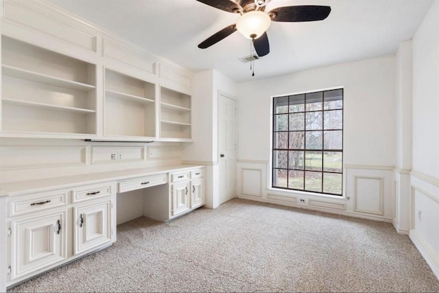 unfurnished office featuring ceiling fan, light colored carpet, and built in desk