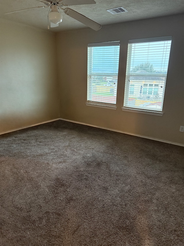 empty room with ceiling fan, a textured ceiling, and dark colored carpet