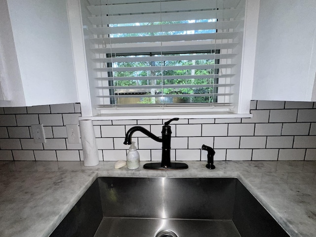 interior details with light stone counters, a sink, and tasteful backsplash