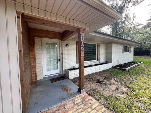 doorway to property featuring covered porch and brick siding