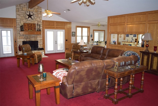 carpeted living room featuring french doors, lofted ceiling with beams, wooden walls, ceiling fan, and a fireplace