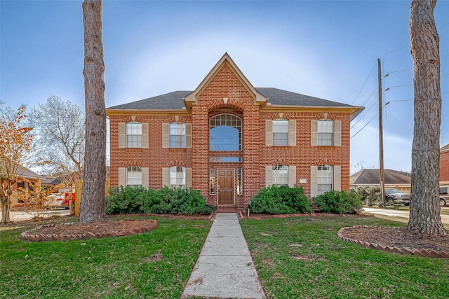 view of front of property featuring roof with shingles, a front lawn, and brick siding