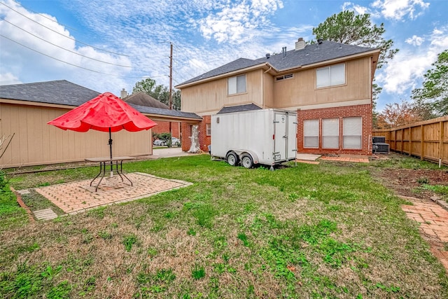 rear view of house featuring an outbuilding, a patio, brick siding, fence, and a yard