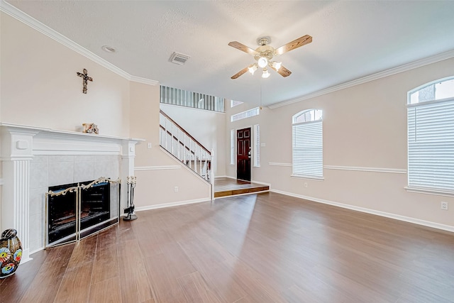 unfurnished living room featuring stairs, a tiled fireplace, wood finished floors, and a wealth of natural light