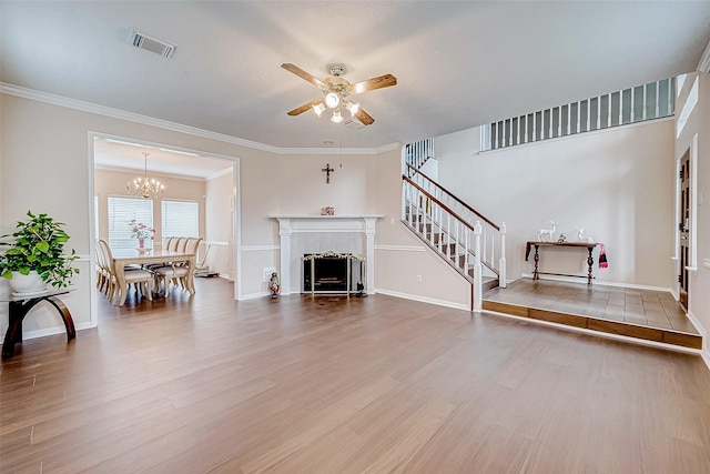 living area featuring ceiling fan with notable chandelier, a fireplace, wood finished floors, visible vents, and stairs