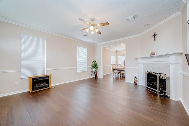 unfurnished living room with crown molding, visible vents, a tiled fireplace, ceiling fan, and wood finished floors