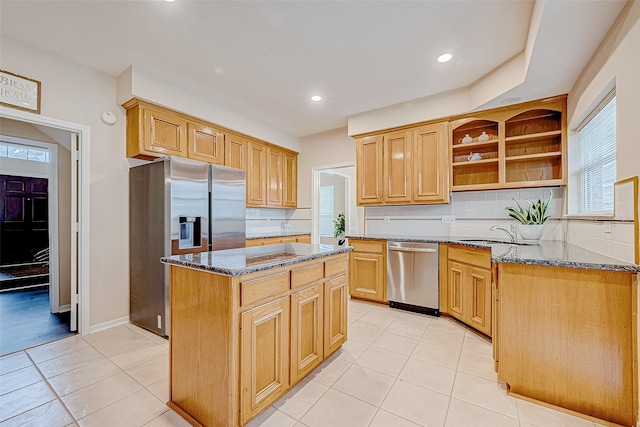 kitchen featuring dark stone counters, a center island, stainless steel appliances, open shelves, and a sink