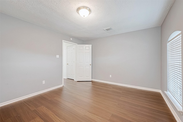 spare room with light wood-type flooring, baseboards, visible vents, and a textured ceiling