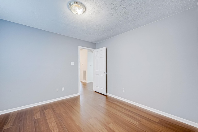 unfurnished room featuring visible vents, a textured ceiling, baseboards, and wood finished floors