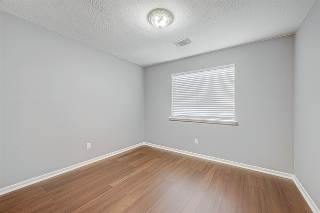 spare room with visible vents, a textured ceiling, baseboards, and wood finished floors