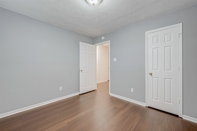 unfurnished bedroom with a textured ceiling, wood finished floors, and baseboards