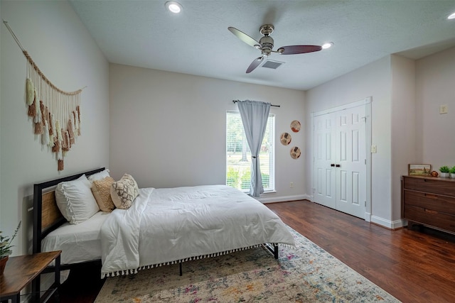 bedroom with a textured ceiling, ceiling fan, dark wood-type flooring, and a closet