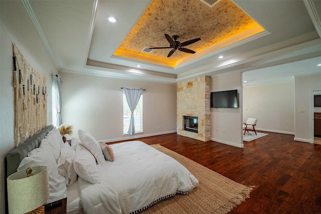 bedroom featuring dark wood-type flooring, a raised ceiling, crown molding, ceiling fan, and a fireplace