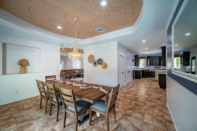 dining space with a tray ceiling, a chandelier, and ornamental molding