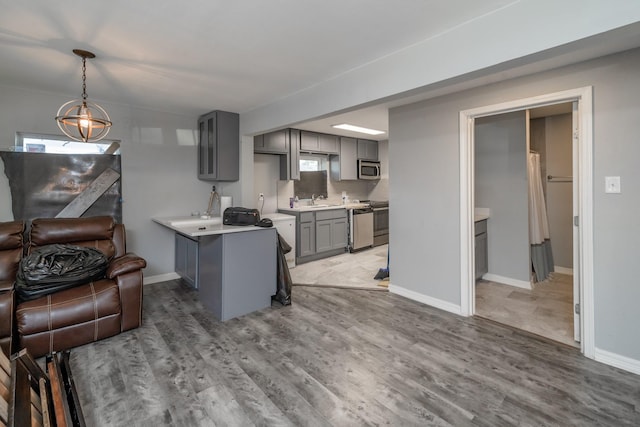 kitchen with gray cabinetry, hardwood / wood-style floors, appliances with stainless steel finishes, decorative light fixtures, and kitchen peninsula