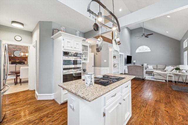 kitchen with light stone countertops, vaulted ceiling, ceiling fan, white cabinets, and a center island