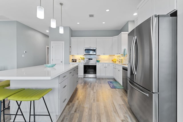 kitchen featuring pendant lighting, white cabinets, appliances with stainless steel finishes, tasteful backsplash, and a breakfast bar area