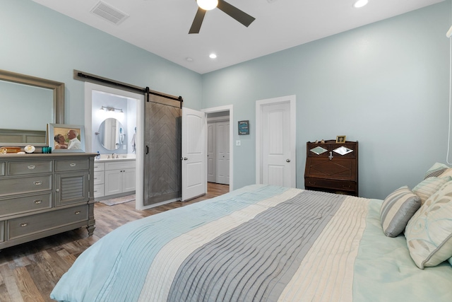 bedroom featuring dark hardwood / wood-style flooring, ceiling fan, sink, a barn door, and connected bathroom