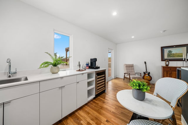 kitchen featuring sink, light hardwood / wood-style flooring, white cabinetry, and beverage cooler