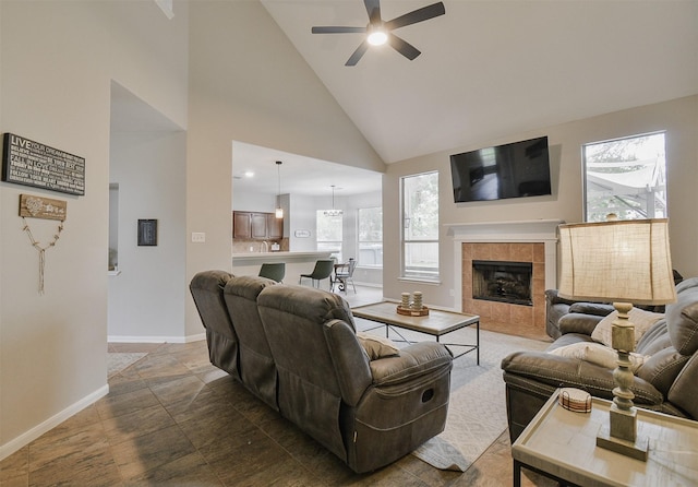 living room featuring a tiled fireplace, ceiling fan, and high vaulted ceiling