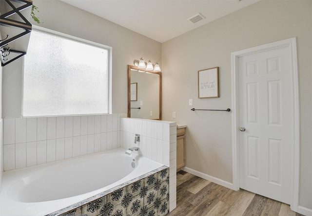 bathroom with tiled tub, hardwood / wood-style floors, and vanity