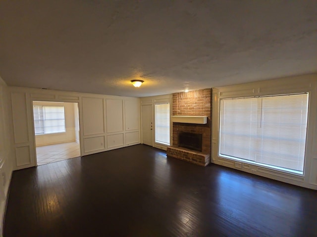 unfurnished living room featuring a textured ceiling, a brick fireplace, and dark wood-type flooring