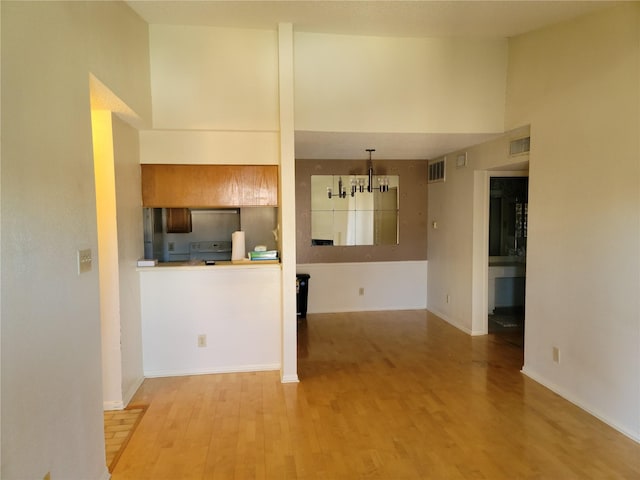 kitchen with range, light hardwood / wood-style flooring, a notable chandelier, a high ceiling, and hanging light fixtures