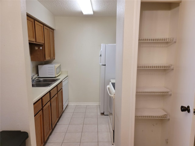 kitchen with a textured ceiling, sink, light tile patterned floors, and white appliances