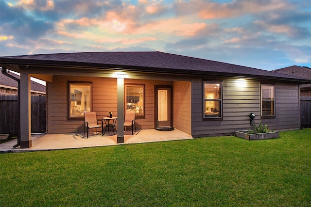 back house at dusk featuring a patio and a lawn