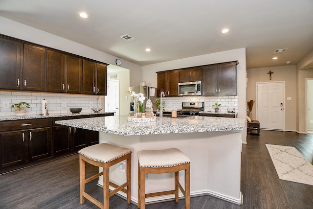 kitchen featuring dark brown cabinetry, sink, dark wood-type flooring, a center island with sink, and appliances with stainless steel finishes