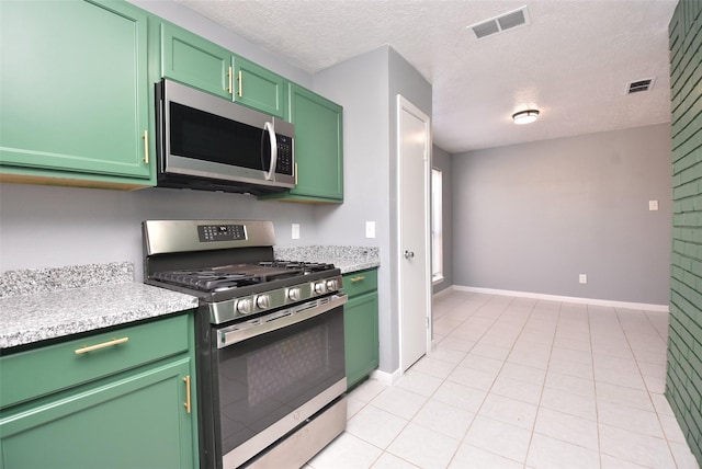 kitchen with appliances with stainless steel finishes, light stone counters, a textured ceiling, light tile patterned floors, and green cabinetry