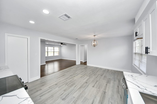 unfurnished living room with ceiling fan with notable chandelier and light hardwood / wood-style flooring