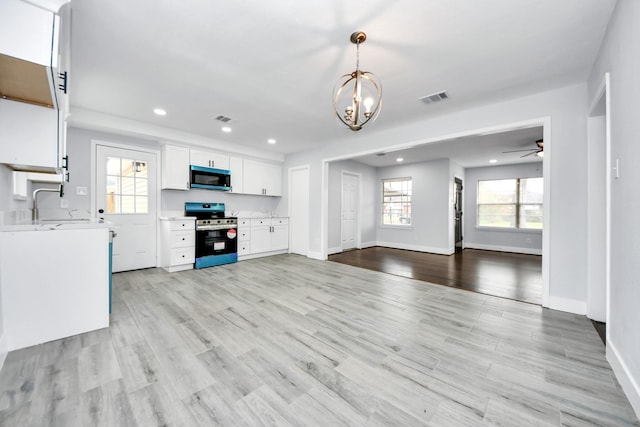 unfurnished living room with ceiling fan with notable chandelier, light hardwood / wood-style floors, sink, and a wealth of natural light