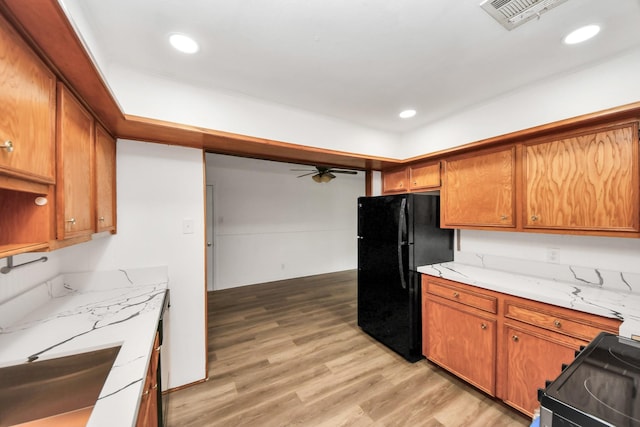 kitchen with light wood-type flooring, black fridge, ceiling fan, sink, and range