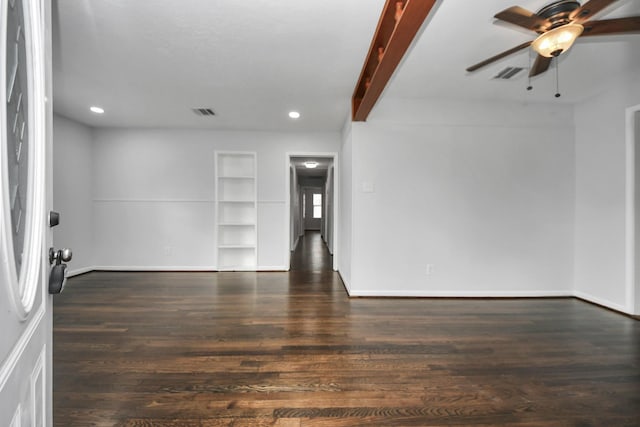 empty room featuring beam ceiling, built in features, ceiling fan, and dark wood-type flooring