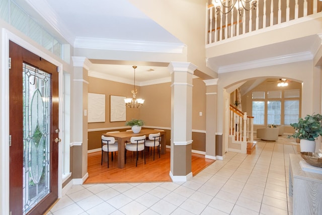 entryway featuring ceiling fan with notable chandelier, light tile patterned floors, ornamental molding, and ornate columns