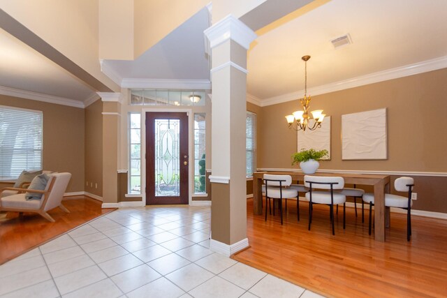 foyer entrance featuring light tile patterned floors, decorative columns, an inviting chandelier, and ornamental molding